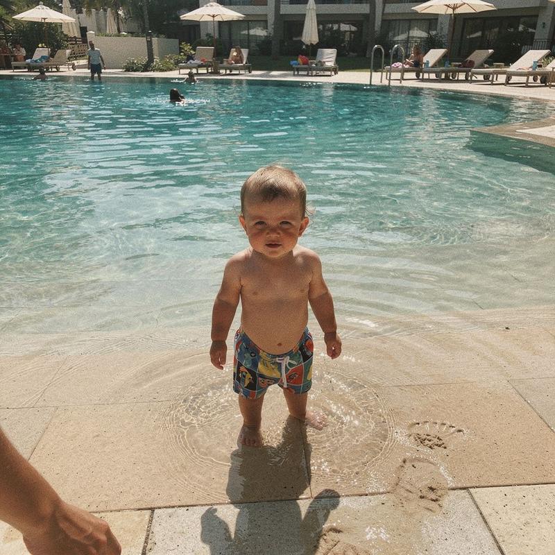 A young child standing in ankle-deep water at the shallow end of a resort children's pool